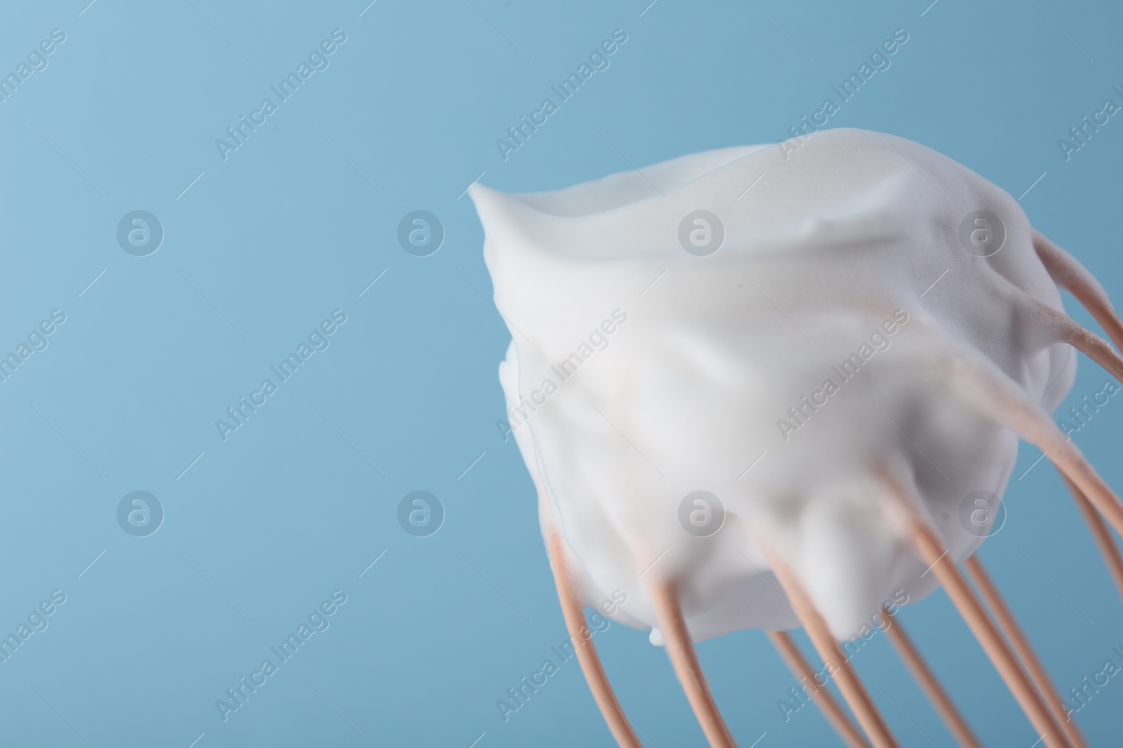 Photo of Whisk with whipped cream on light blue background, closeup. Space for text