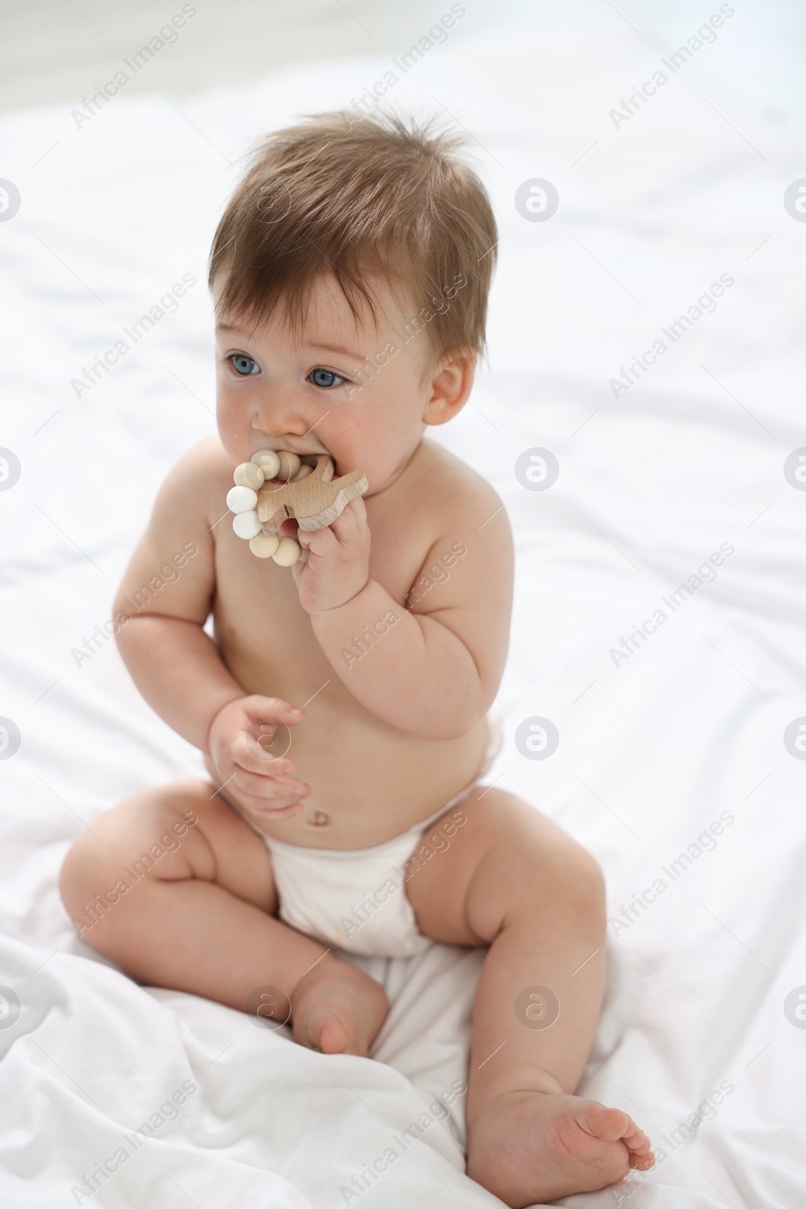 Photo of Cute baby boy with wooden teether sitting on bed