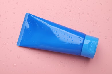 Photo of Wet tube of face cleansing product on pink background, top view