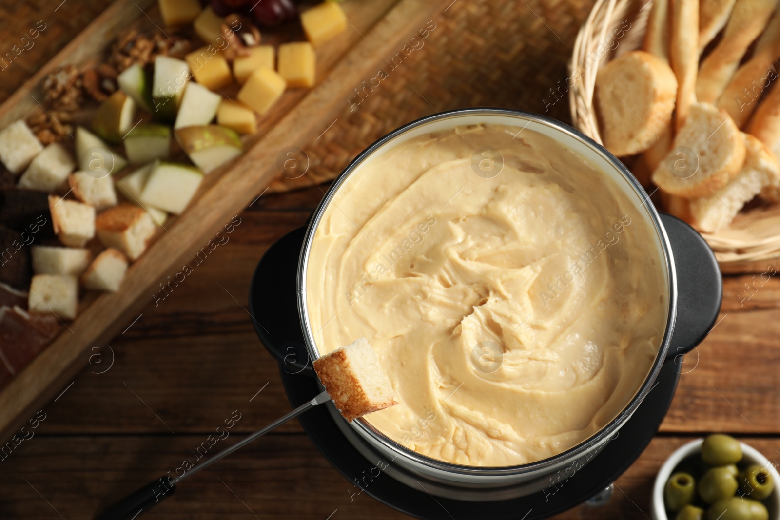 Photo of Fondue with tasty melted cheese, fork and different snacks on wooden table, top view