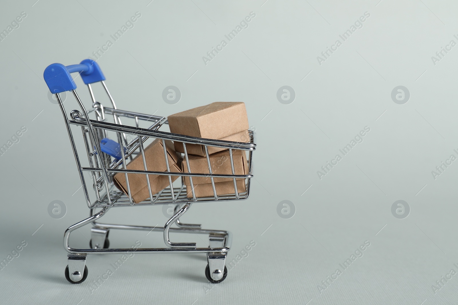 Photo of Small metal shopping cart with cardboard boxes on light background, space for text