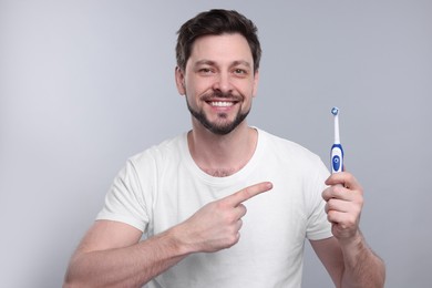 Photo of Happy man holding electric toothbrush on light grey background