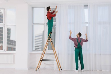 Photo of Workers in uniform hanging window curtain indoors