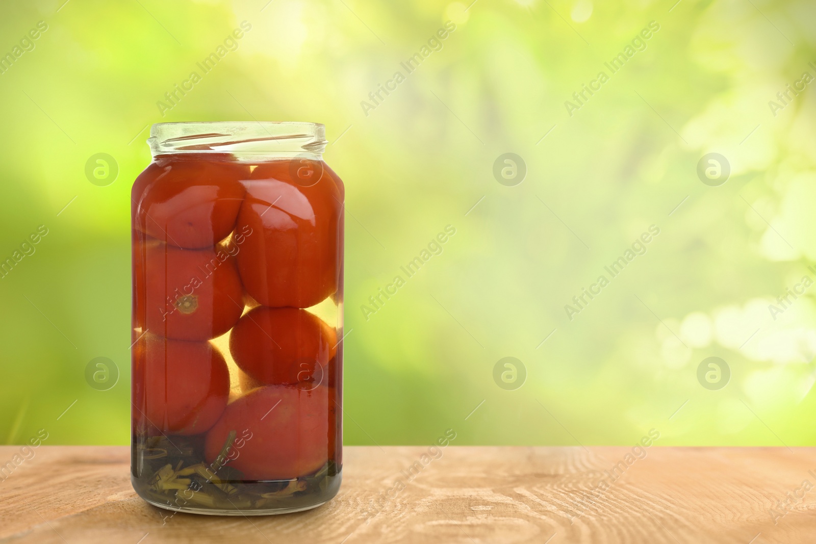 Image of Jar of pickled tomatoes on wooden table against blurred background, space for text