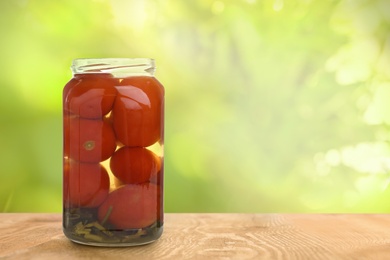 Image of Jar of pickled tomatoes on wooden table against blurred background, space for text