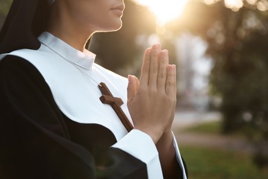 Young nun with hands clasped together praying outdoors on sunny day, closeup