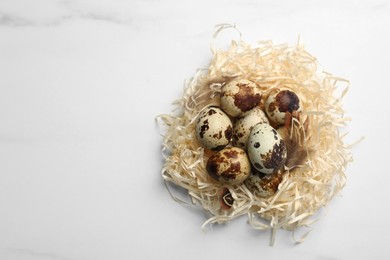 Photo of Nest with quail eggs on white marble table, top view. Space for text