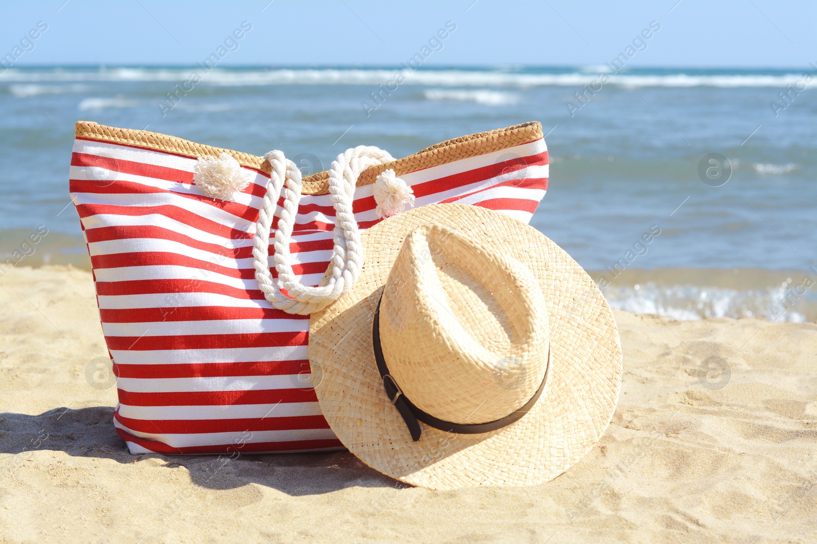 Photo of Stylish striped bag with straw hat on sandy beach near sea