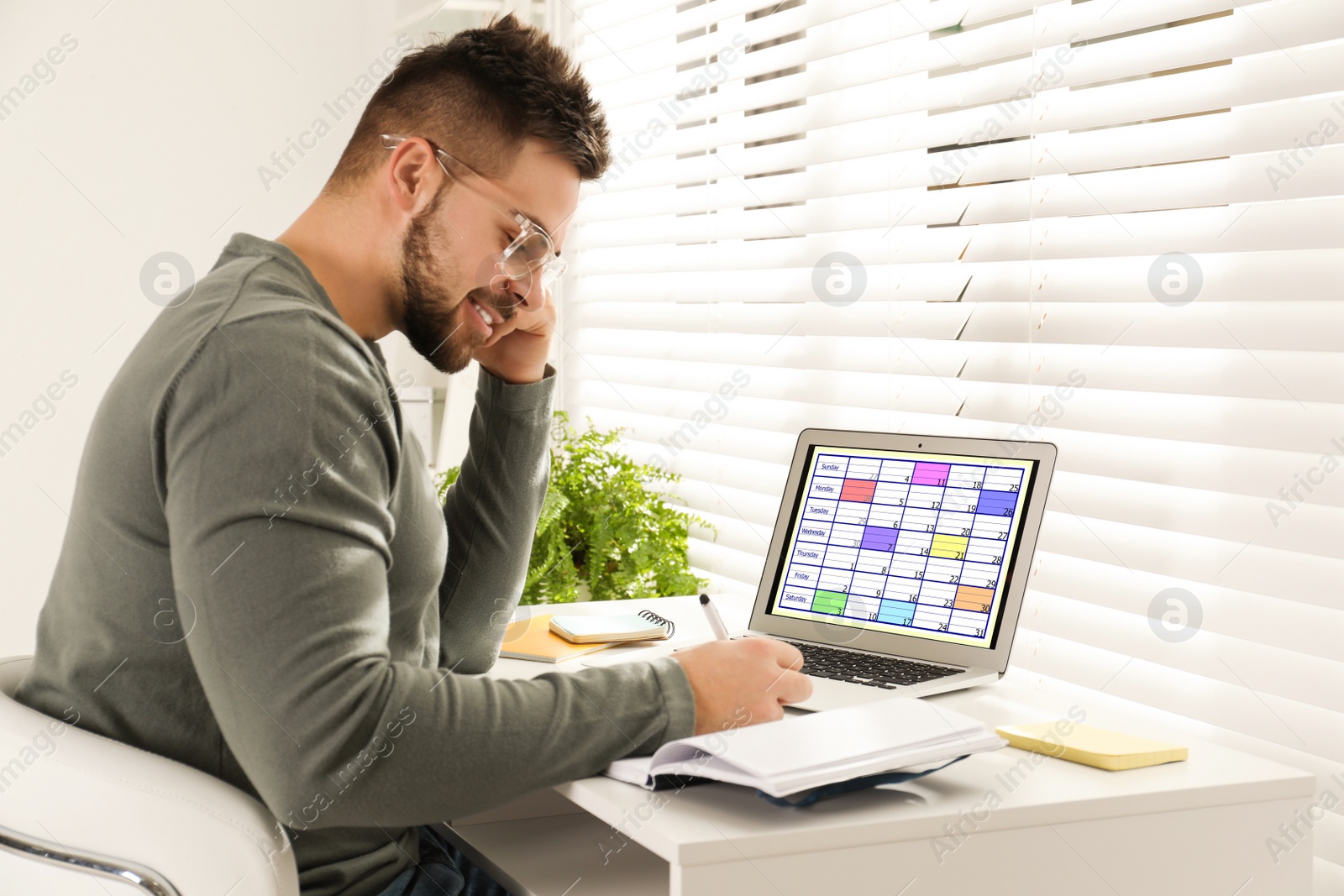 Photo of Young man using calendar app on laptop in office