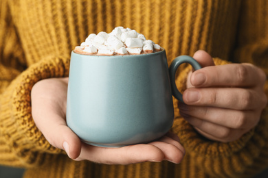 Photo of Woman holding cup of aromatic cocoa with marshmallows, closeup