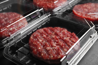 Photo of Plastic containers with raw meat cutlets for burger on table, closeup