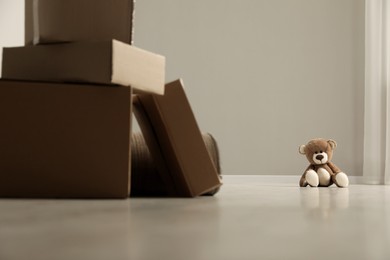 Cute lonely teddy bear on floor near boxes indoors