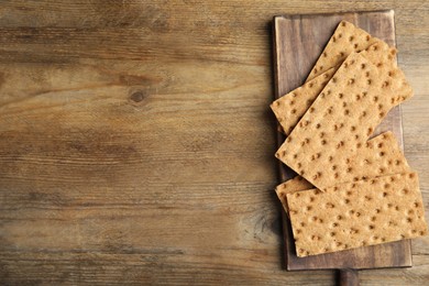 Photo of Board with fresh rye crispbreads on wooden table, top view. Space for text