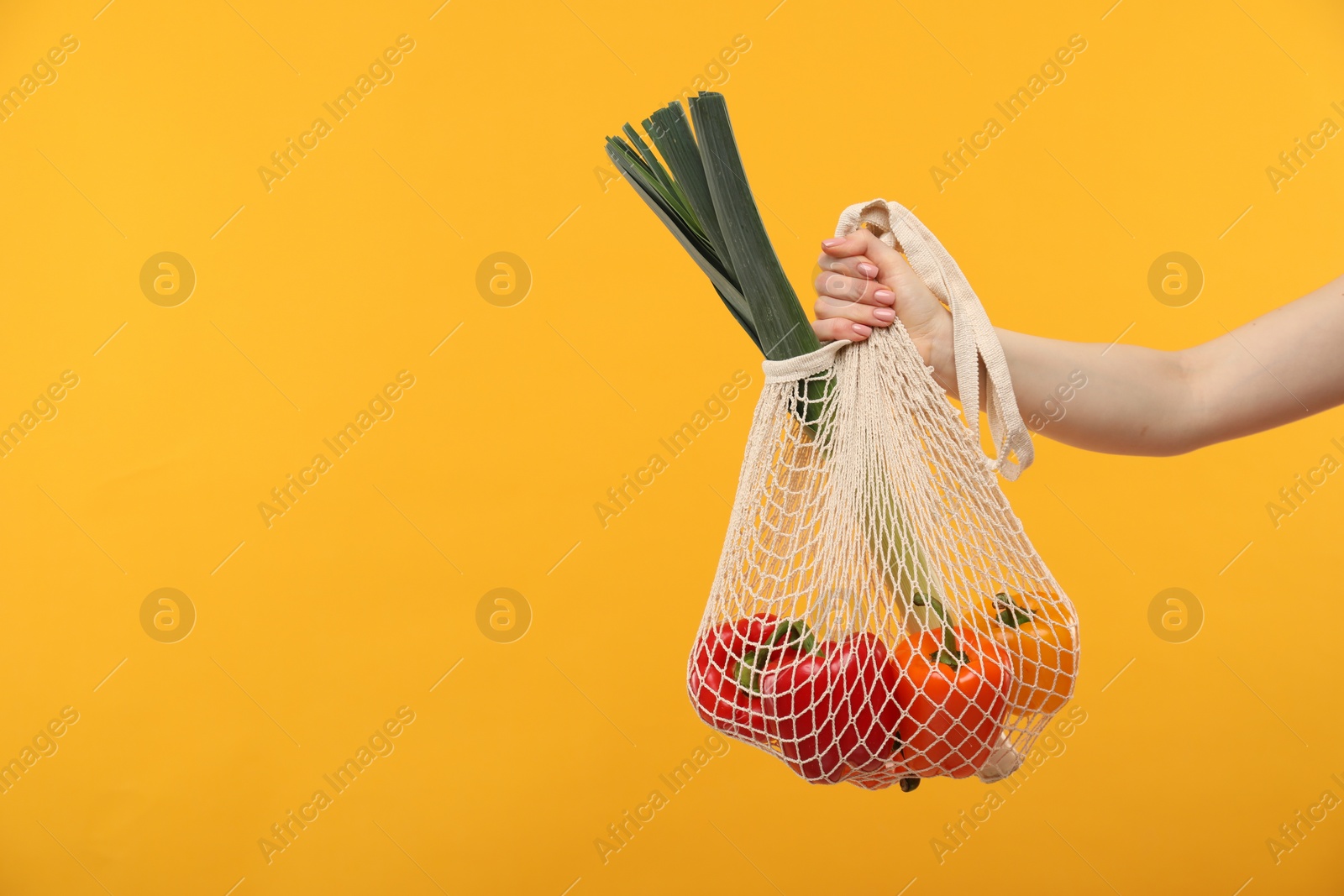 Photo of Woman with string bag of fresh vegetables on orange background, closeup. Space for text