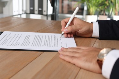 Photo of Businessman signing contract at wooden table indoors, closeup