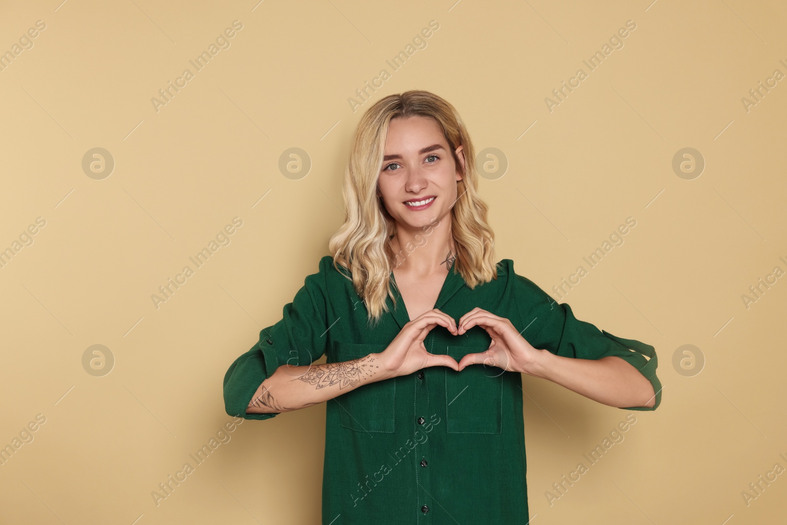 Photo of Happy volunteer making heart with her hands on beige background