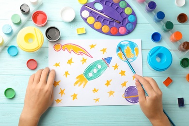 Girl painting picture of spaceship on table, top view