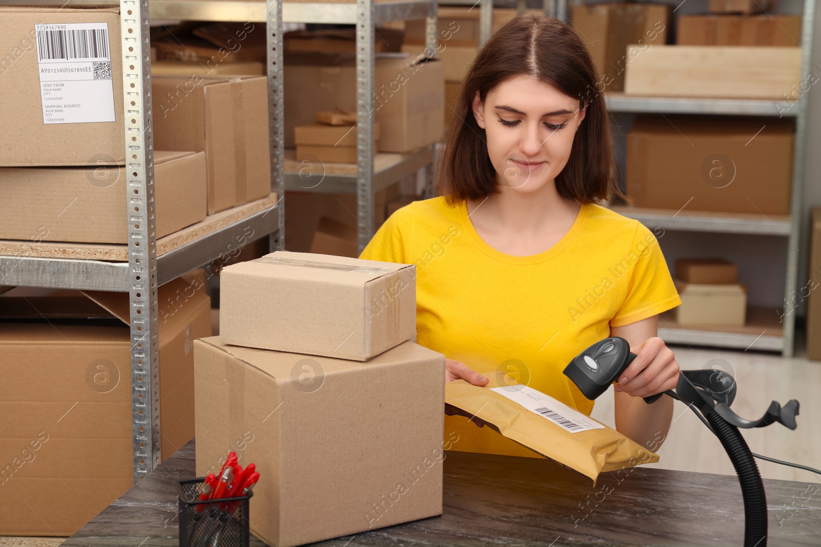 Photo of Post office worker with scanner reading parcel barcode at counter indoors