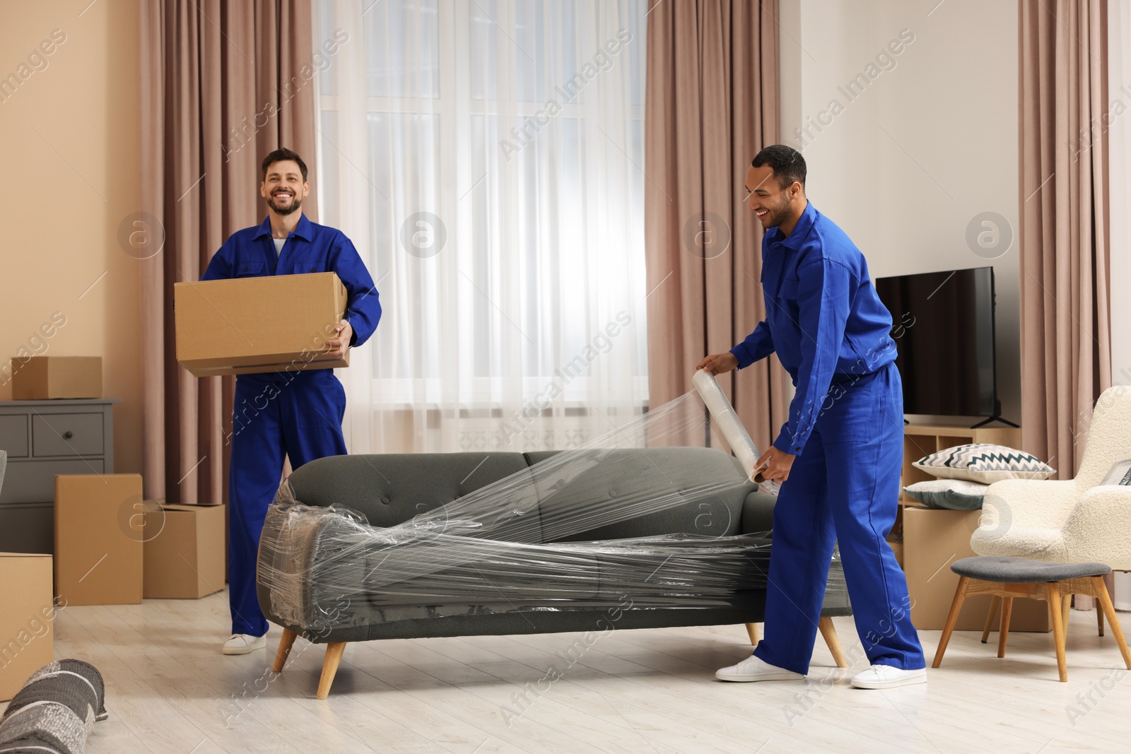 Photo of Male movers with cardboard box and sofa in new house