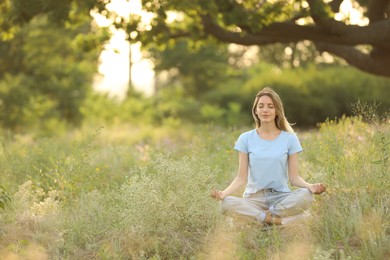 Young woman meditating on green grass in park, space for text