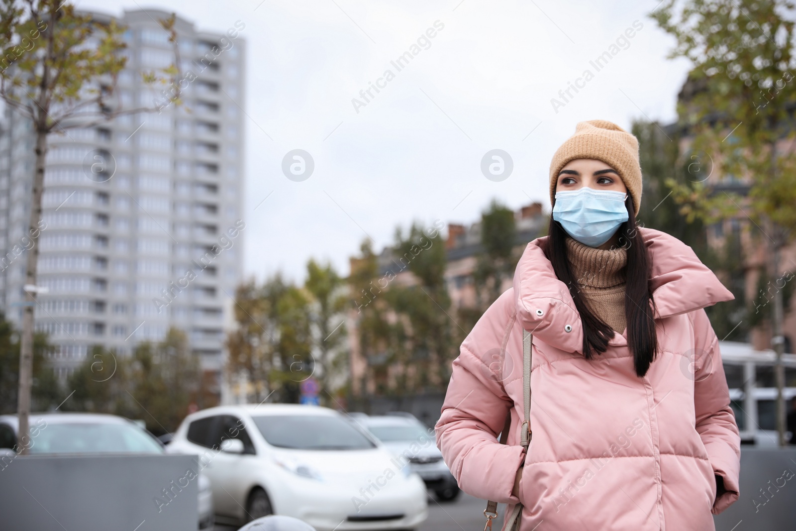 Photo of Young woman in medical face mask walking outdoors. Personal protection during COVID-19 pandemic