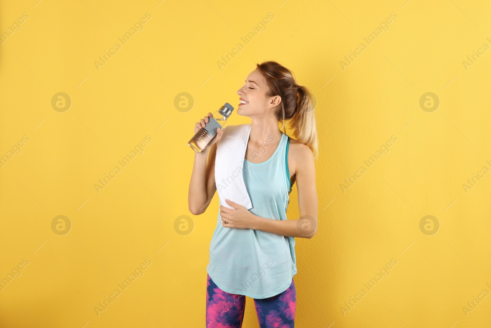 Photo of Beautiful young woman in sportswear with towel and bottle of water on color background