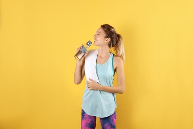 Beautiful young woman in sportswear with towel and bottle of water on color background