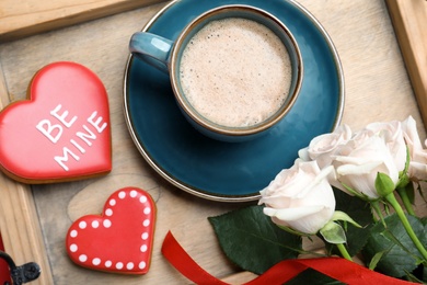 Romantic breakfast with coffee, heart shaped cookies and roses on wooden tray, flat lay. Valentine's day celebration