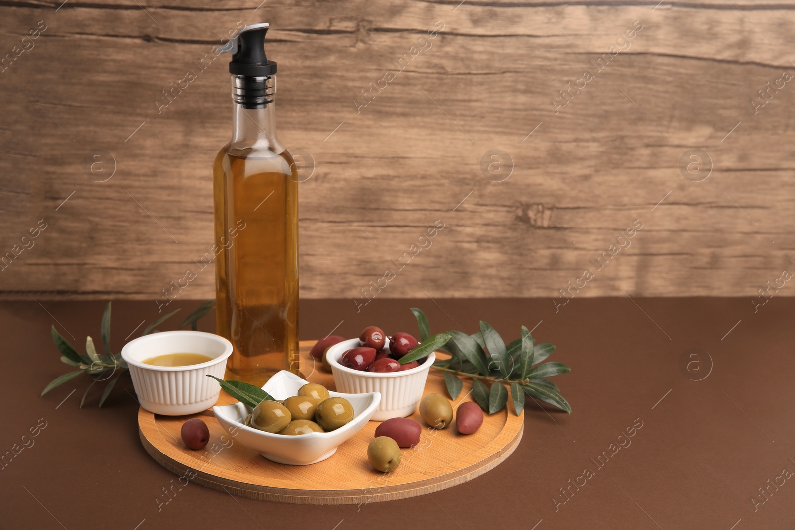Photo of Oil, olives and tree twigs on brown table, space for text