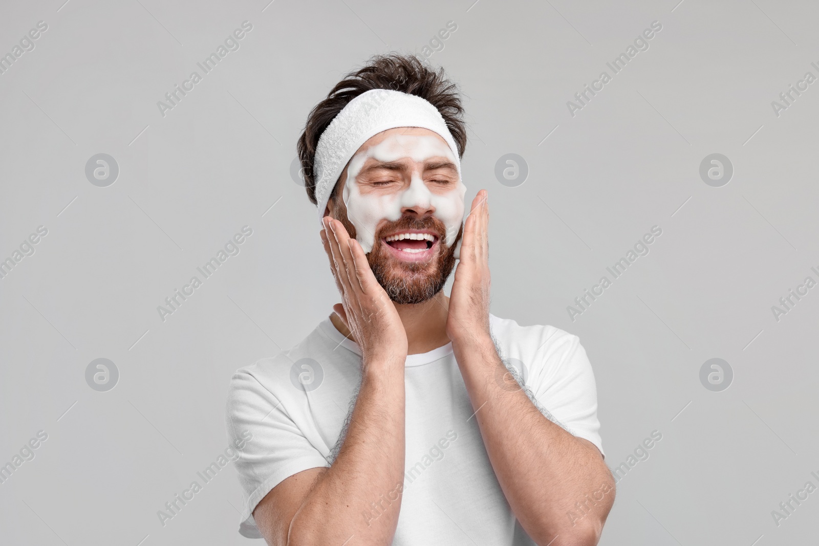 Photo of Man with headband washing his face on light grey background