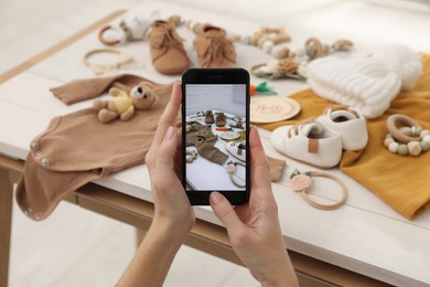Photo of Woman taking picture of baby clothes at white wooden table, closeup