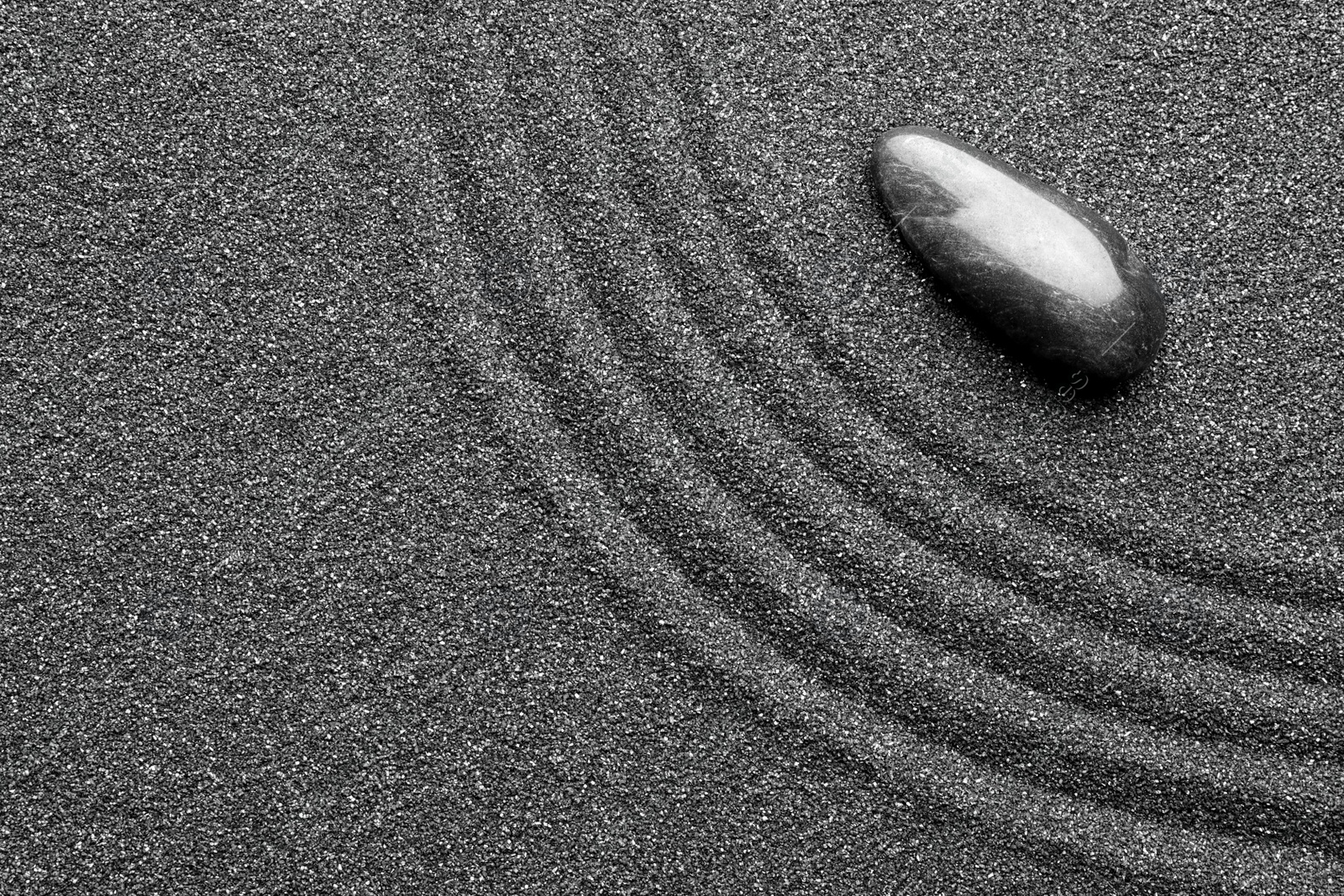 Photo of Zen garden stone on black sand with pattern, top view