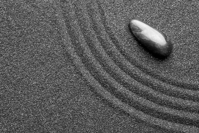 Photo of Zen garden stone on black sand with pattern, top view