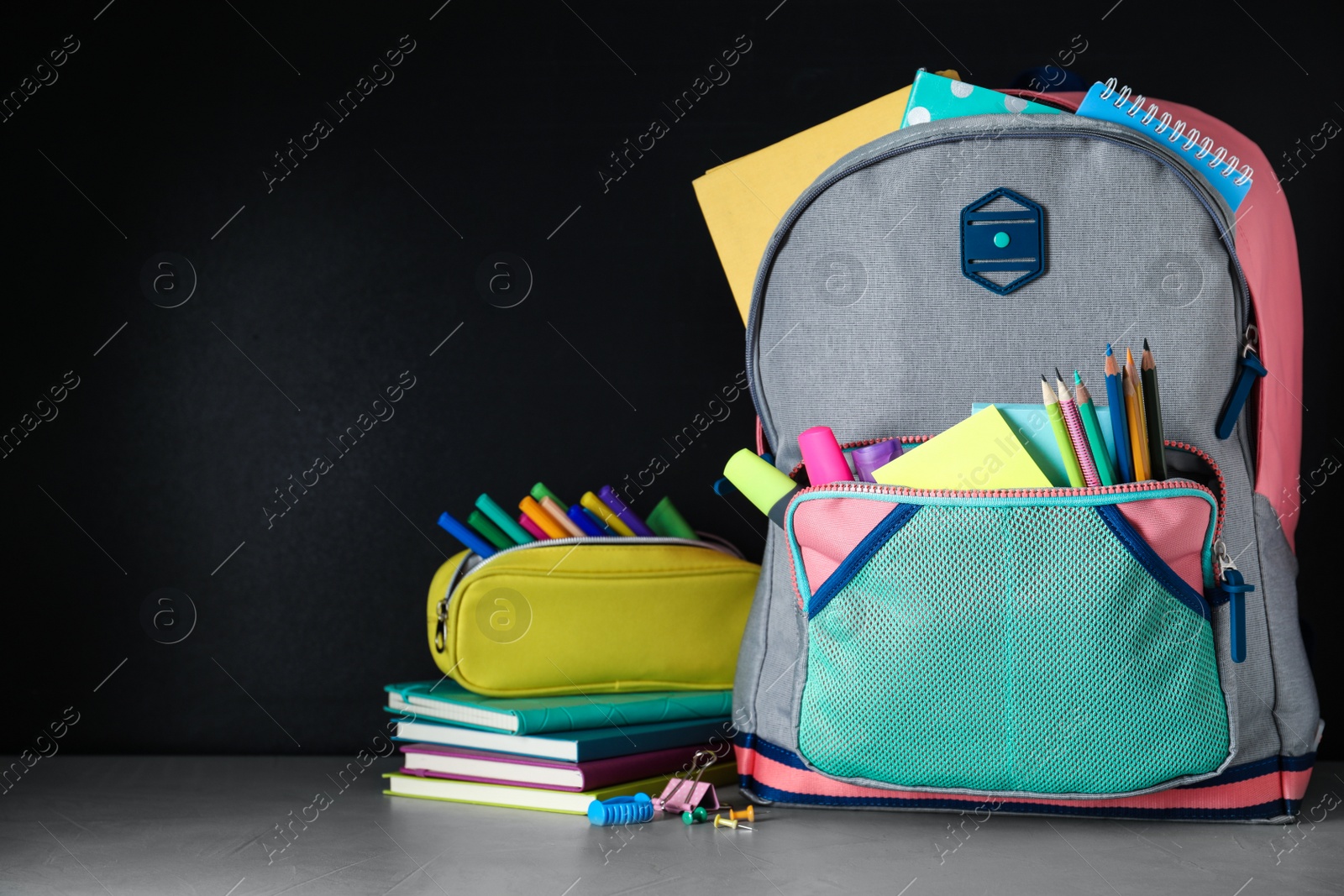 Photo of Bright backpack with school stationery on grey stone table against black background