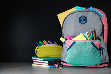Photo of Bright backpack with school stationery on grey stone table against black background