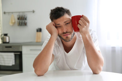 Photo of Sleepy man with cup of drink at home in morning