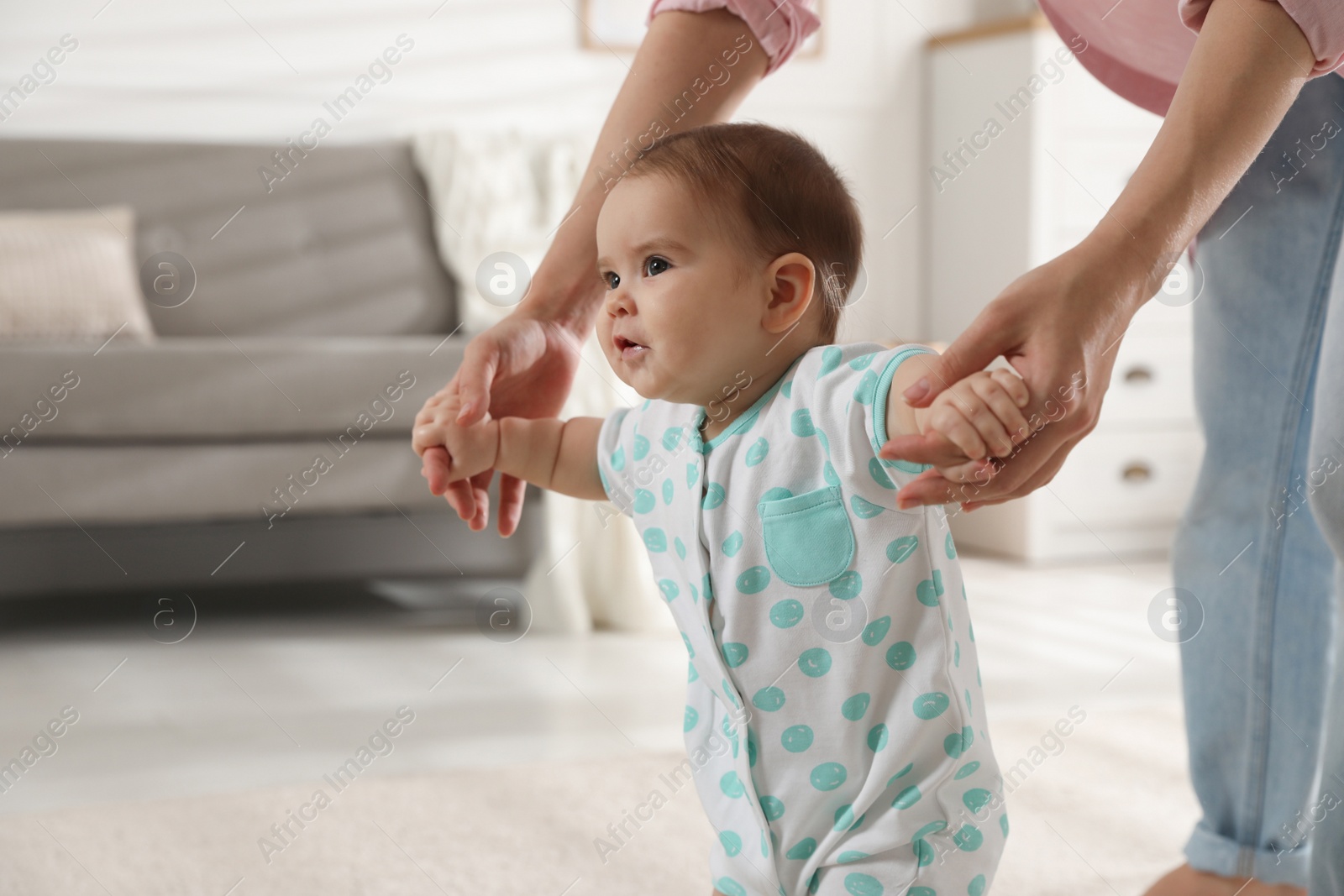 Photo of Mother supporting her baby daughter while she learning to walk at home