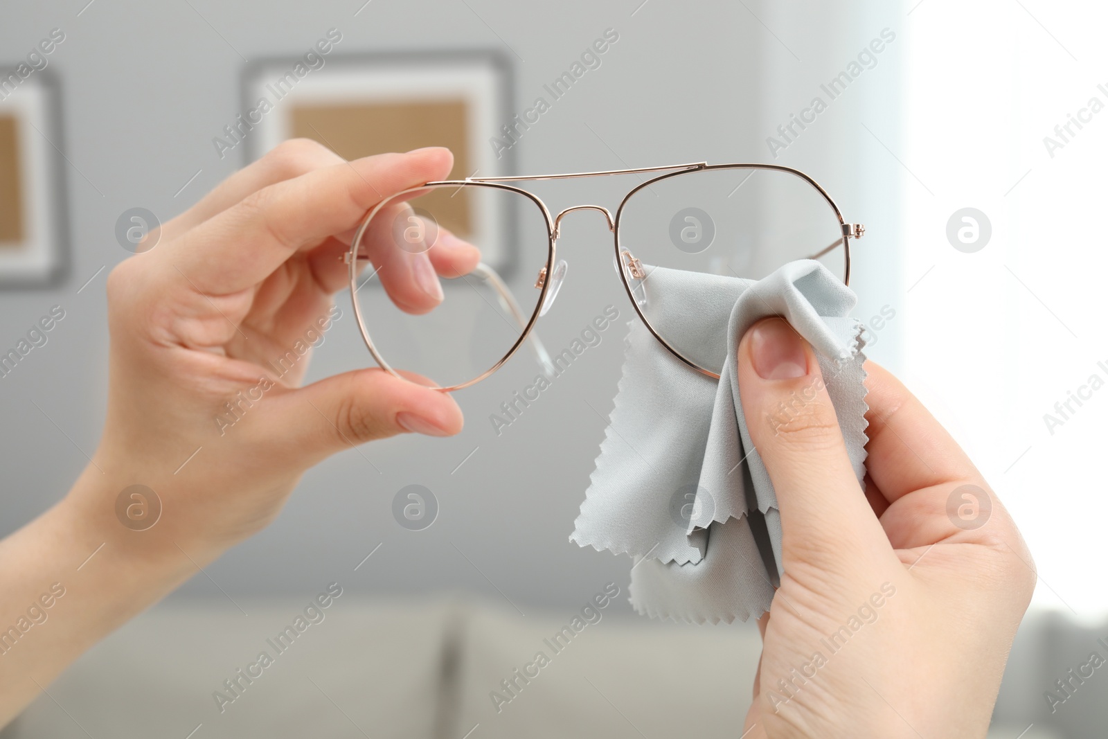 Photo of Woman cleaning glasses with microfiber cloth indoors, closeup