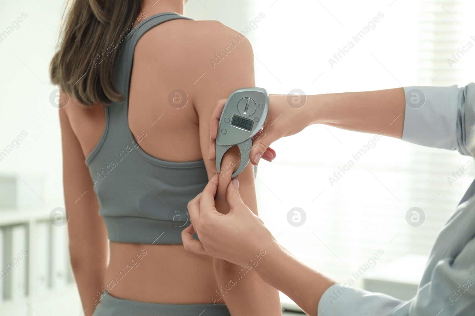 Photo of Nutritionist measuring woman's fat layer with caliper indoors, closeup