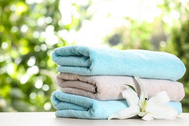 Photo of Stack of clean soft towels and flower on table against blurred background