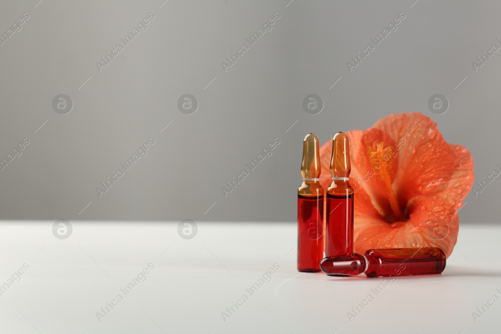 Photo of Skincare ampoules and hibiscus flower on white table. Space for text