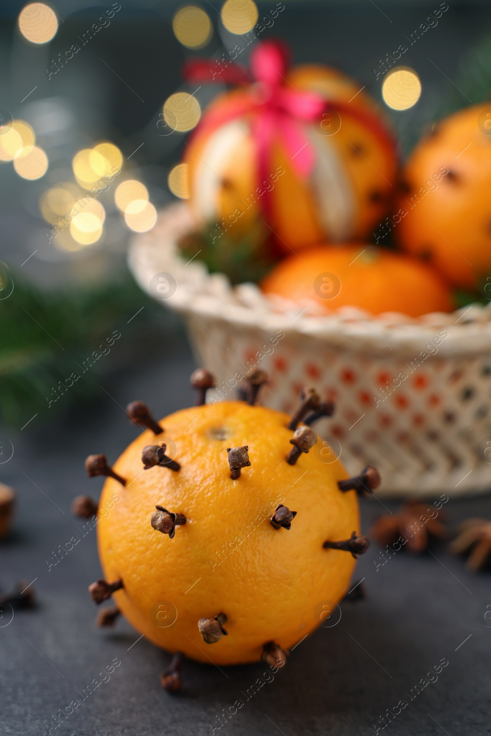 Photo of Pomander balls made of tangerines with cloves on grey table against blurred festive lights