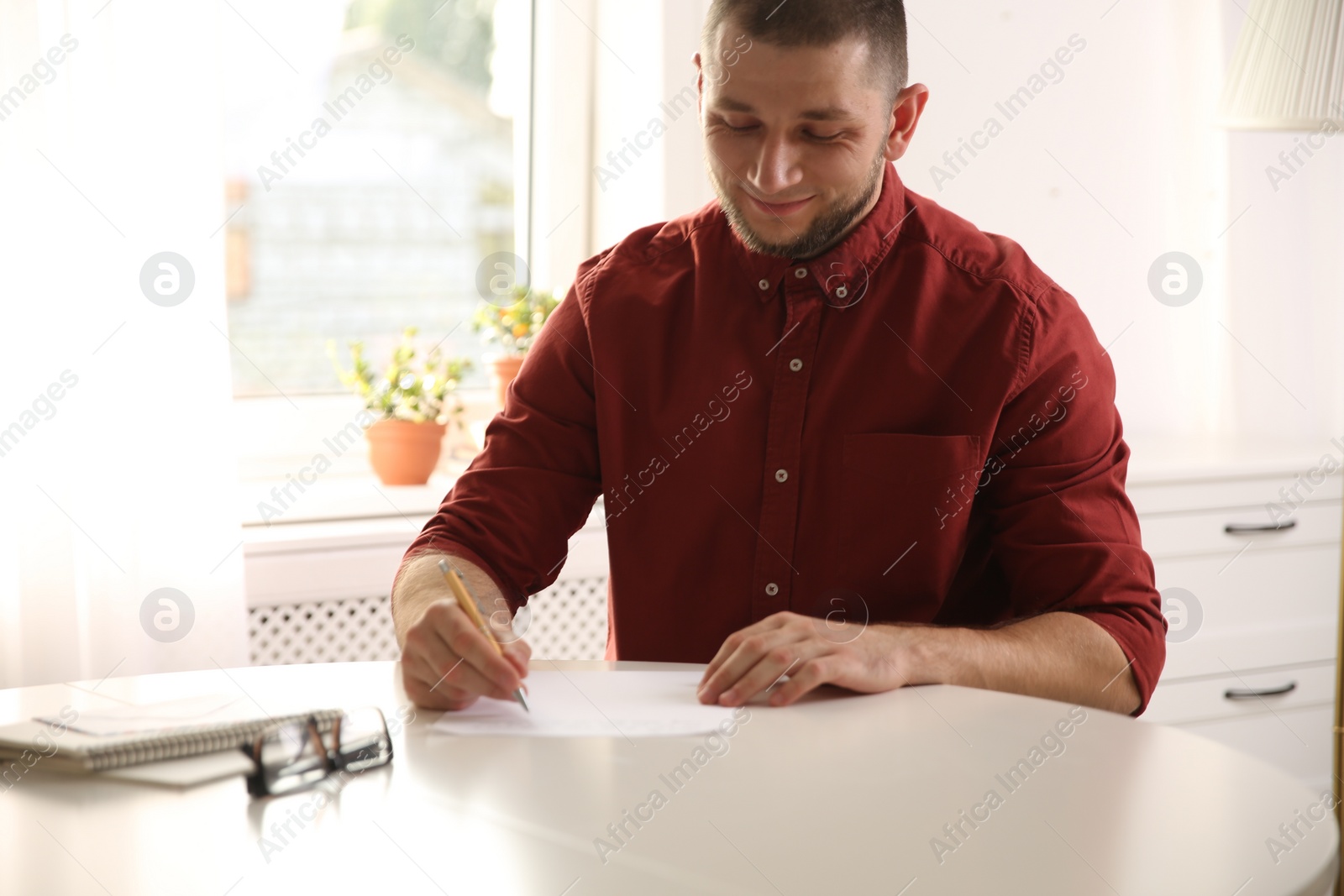 Photo of Man writing letter at white table in room