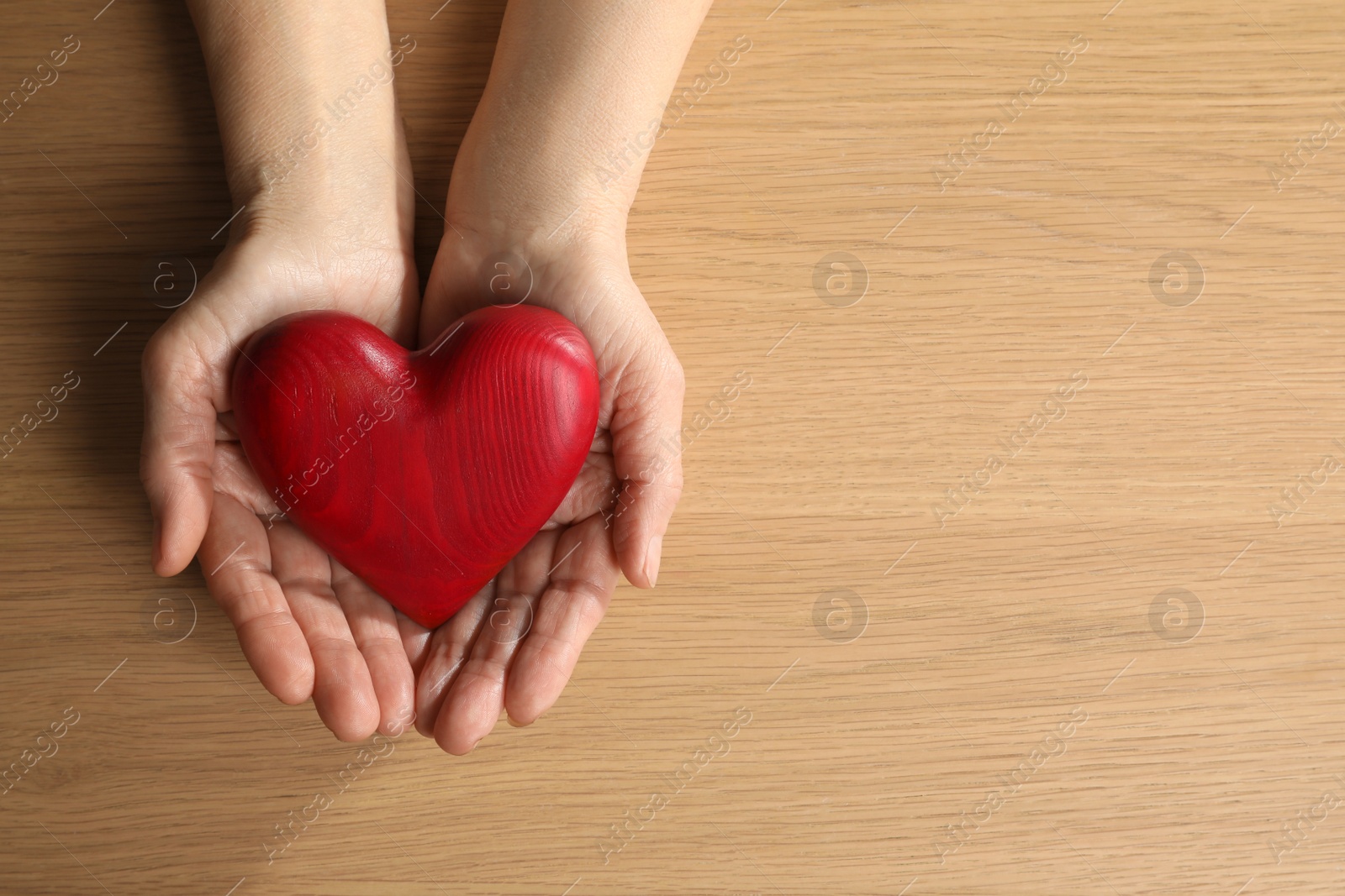 Photo of Elderly woman holding red heart in hands at wooden table, top view. Space for text