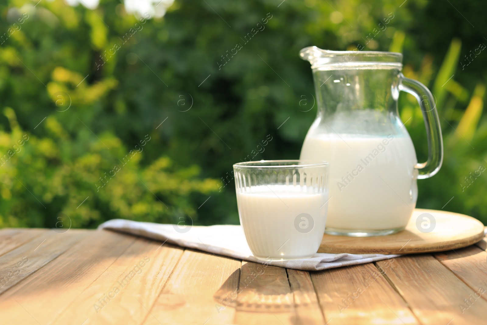 Photo of Glass and jug of tasty fresh milk on wooden table outdoors, space for text