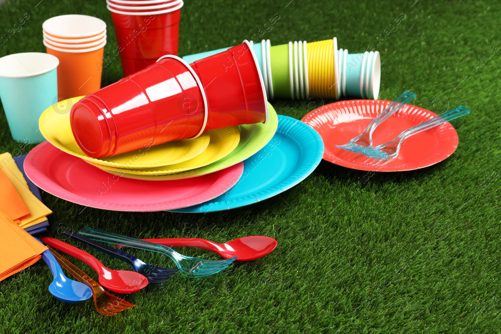 Photo of Disposable tableware on green artificial grass. Space for text