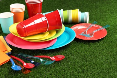 Photo of Disposable tableware on green artificial grass. Space for text