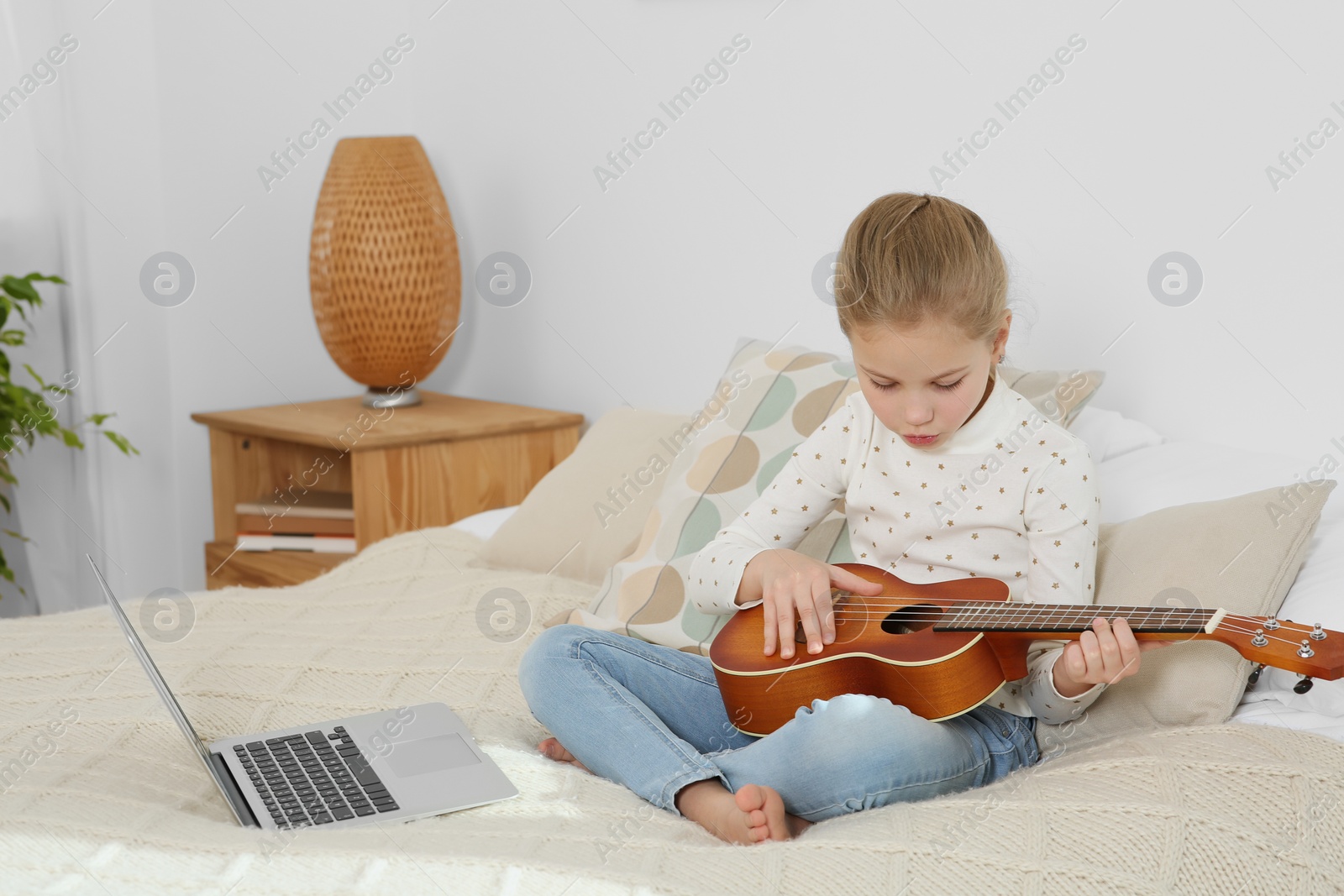 Photo of Little girl learning to play ukulele with online music course at home. Space for text