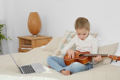 Little girl learning to play ukulele with online music course at home. Space for text