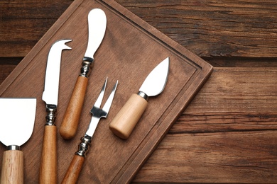 Photo of Cheese knives and fork on wooden table, flat lay